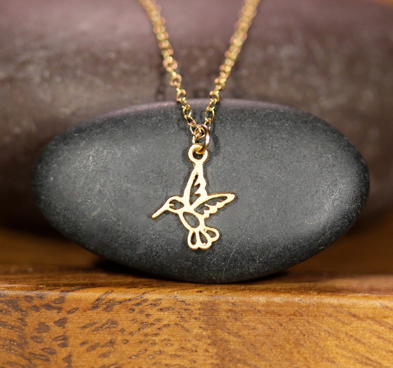 May include: A gold necklace with a delicate hummingbird pendant. The hummingbird is cut out of the metal and has a detailed design.