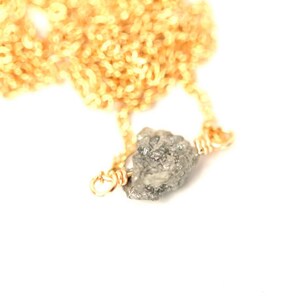 May include: A gold chain necklace with a raw, grey diamond pendant.