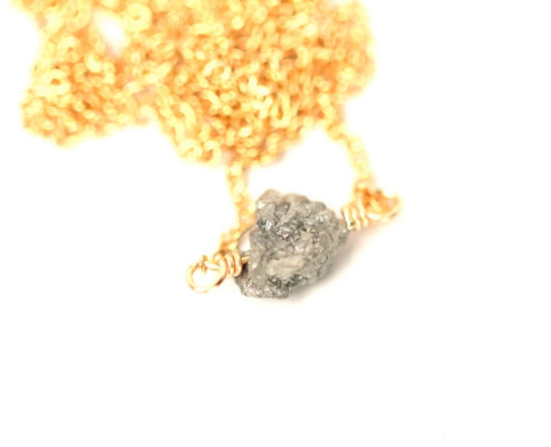 May include: A gold chain necklace with a raw, grey diamond pendant.