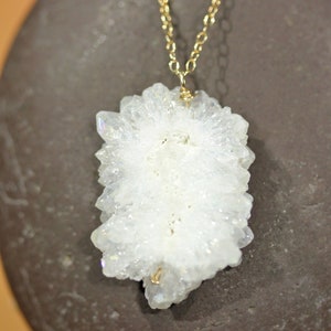 May include: A white crystal pendant with a gold chain. The crystal is a cluster of small, pointed crystals.