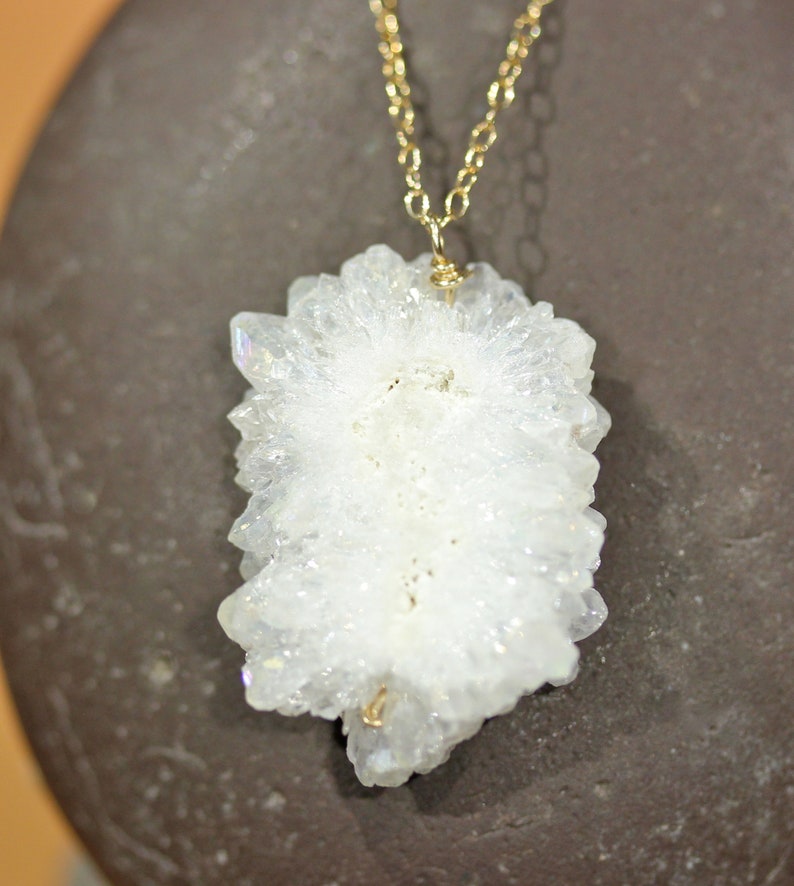 May include: A white crystal pendant with a gold chain. The crystal is a cluster of small, pointed crystals.