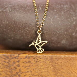May include: A gold chain necklace with a delicate hummingbird pendant. The hummingbird is cut out of metal and has a detailed design.