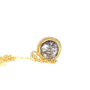May include: A gold chain necklace with a round pendant featuring a clear quartz stone with black inclusions.
