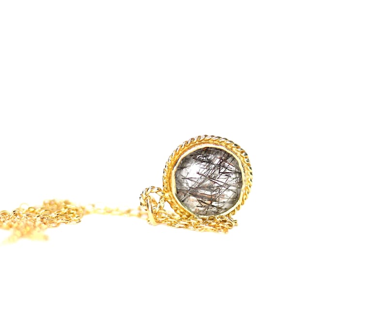 May include: A gold chain necklace with a round pendant featuring a clear quartz stone with black inclusions.