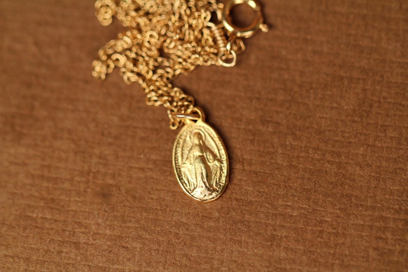 K&ouml;nnte beinhalten: Eine goldene Kettenkette mit einem goldenen Anh&auml;nger, der eine Darstellung der Jungfrau Maria zeigt.