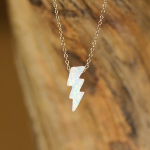May include: A gold chain necklace with a white opal lightning bolt pendant.