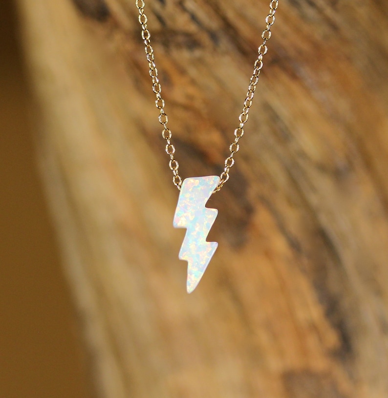 May include: A gold chain necklace with a white opal lightning bolt pendant.
