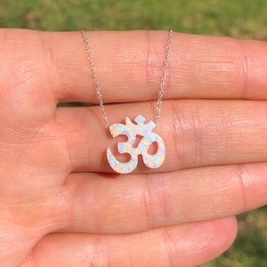 May include: A silver chain necklace with a white opal Om symbol pendant. The pendant is a delicate, detailed design with a sparkly finish.