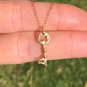 Puede incluir: Un collar de oro con un colgante de llave con un dise&ntilde;o detallado y ornamentado. El colgante de llave est&aacute; unido a una cadena de oro delicada.