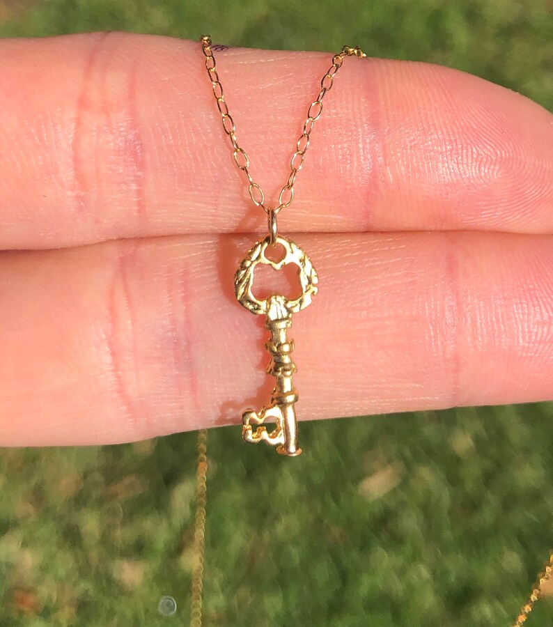 Puede incluir: Un collar de oro con un colgante de llave con un dise&ntilde;o detallado y ornamentado. El colgante de llave est&aacute; unido a una cadena de oro delicada.