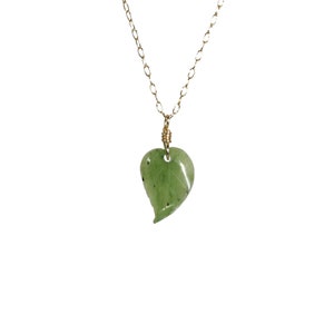 Puede incluir: Un collar de cadena dorada con un colgante de hoja de jade verde. La hoja está tallada en forma de corazón.