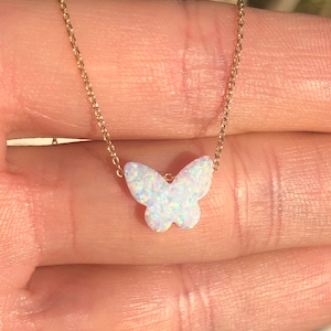May include: A delicate gold chain necklace with a white opal butterfly pendant. The butterfly has a sparkly, iridescent finish.