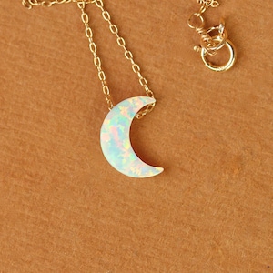 May include: A gold chain necklace with a crescent moon pendant made of iridescent opal.