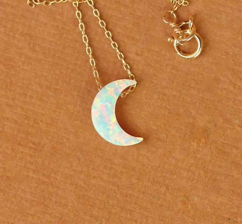 May include: A gold chain necklace with a crescent moon pendant made of iridescent opal.