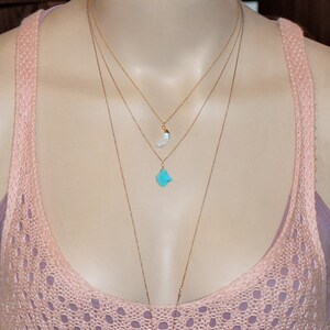 May include: A layered gold necklace with a turquoise stone pendant and a white crescent moon pendant.