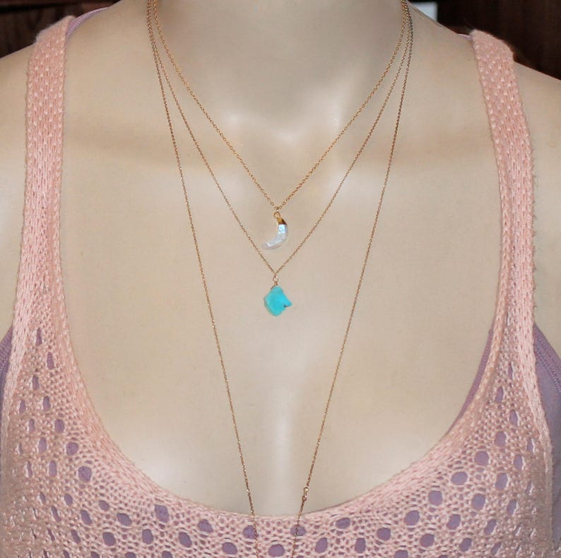 May include: A layered gold necklace with a turquoise stone pendant and a white crescent moon pendant.