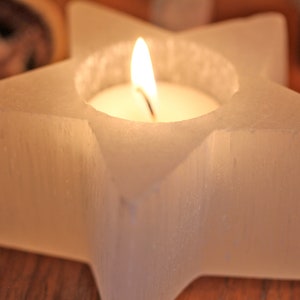 May include: A white star-shaped candle holder with a small white candle burning inside. The holder is made of a textured material and has a smooth, polished finish.