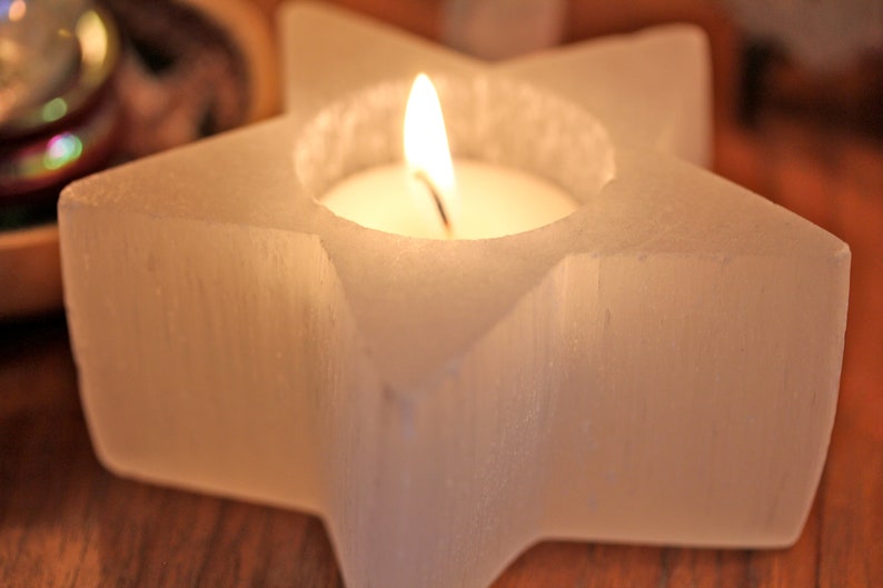 May include: A white star-shaped candle holder with a small white candle burning inside. The holder is made of a textured material and has a smooth, polished finish.