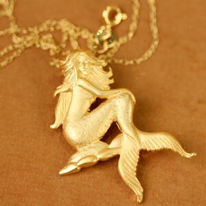 Peut inclure: Un collier en or avec un pendentif en forme de sirène. La sirène est assise sur un rocher avec sa queue enroulée autour d'elle.