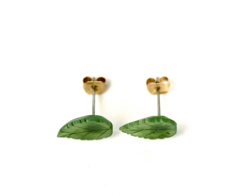 May include: A pair of green jade leaf earrings with gold posts. The leaves are carved with delicate veins.