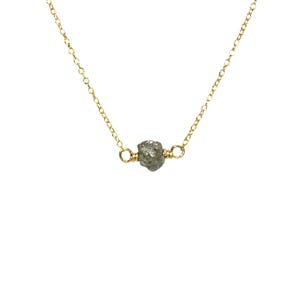 May include: A delicate gold chain necklace with a single, raw, grey diamond pendant.