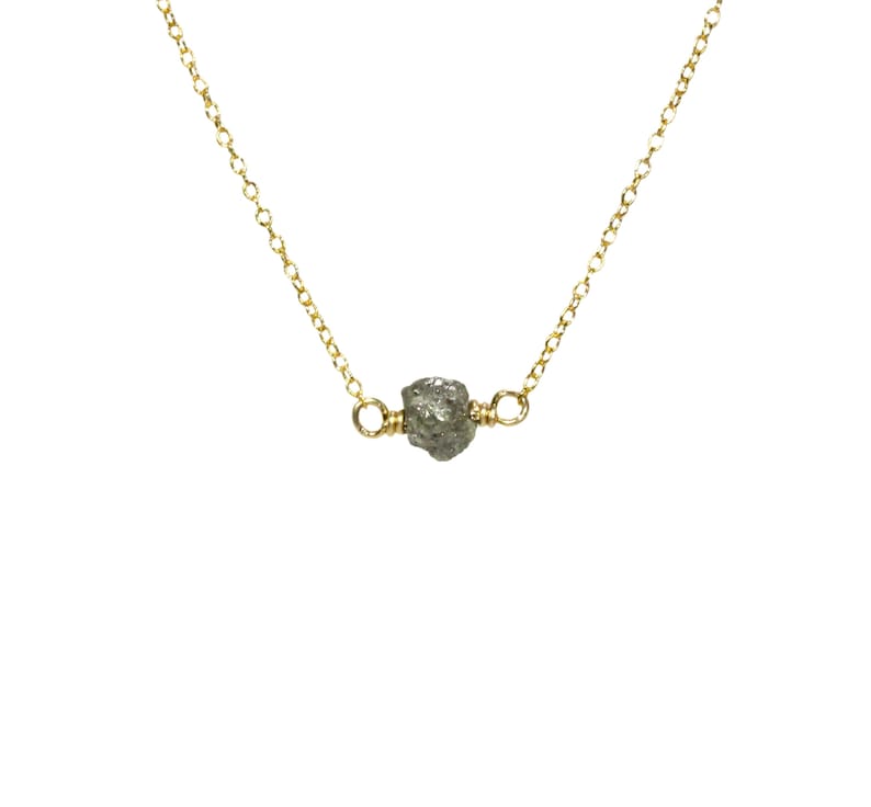 May include: A delicate gold chain necklace with a single, raw, grey diamond pendant.