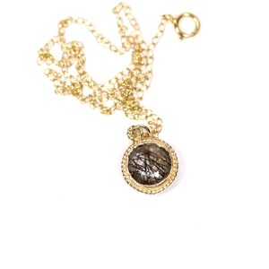 May include: A gold chain necklace with a round pendant featuring a clear stone with black inclusions.