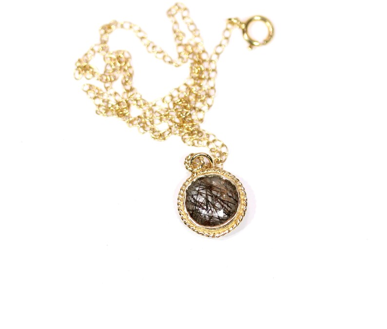 May include: A gold chain necklace with a round pendant featuring a clear stone with black inclusions.