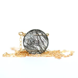 May include: A gold chain necklace with a round, clear quartz pendant featuring black inclusions. The pendant is set in a gold bezel.