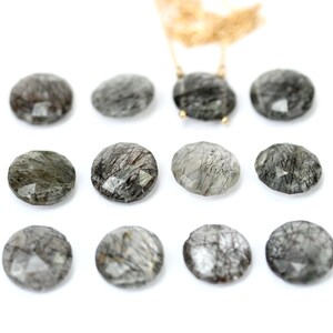 May include: Twelve round, faceted, clear quartz stones with black inclusions. The stones are arranged in three rows of four.