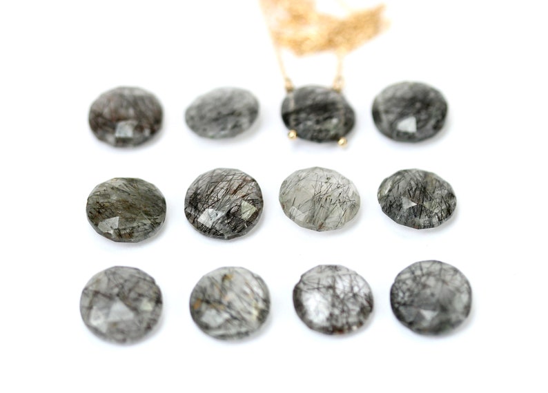 May include: Twelve round, faceted, clear quartz stones with black inclusions. The stones are arranged in three rows of four.