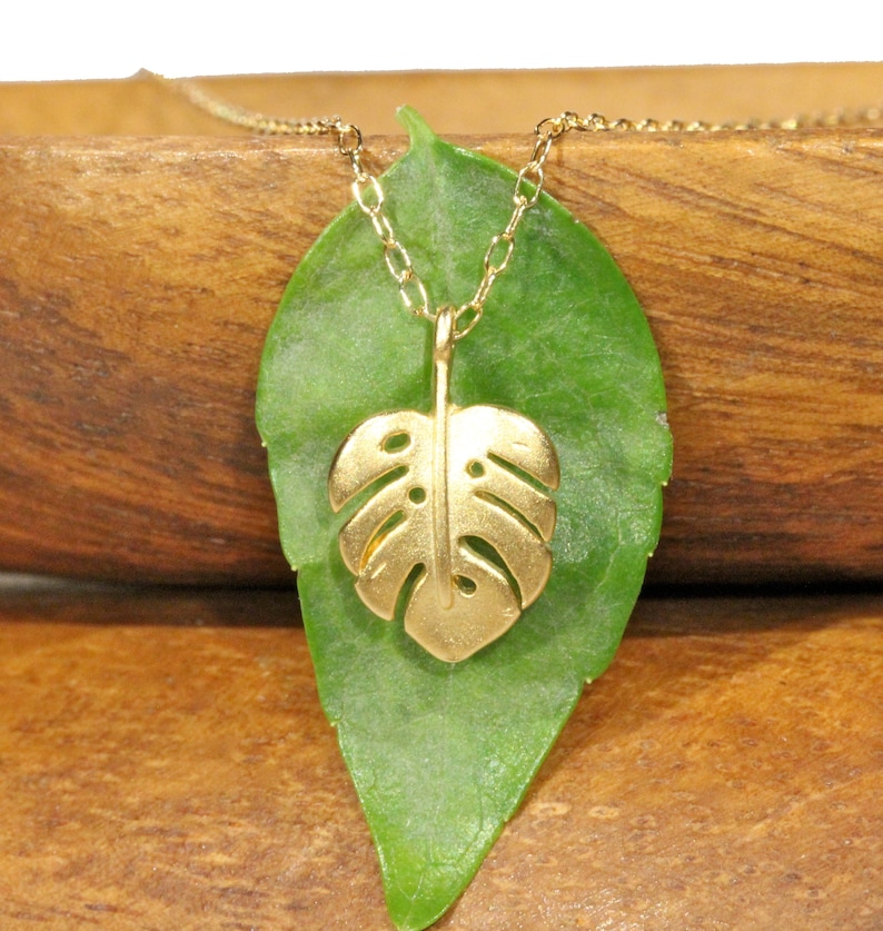Peut inclure: Un collier en or avec une cha&icirc;ne d&eacute;licate et un pendentif en forme de feuille de monstera. Le pendentif est d&eacute;coup&eacute; et pr&eacute;sente un design d&eacute;taill&eacute;.