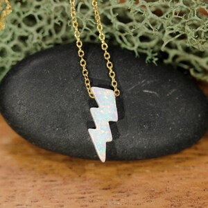 May include: A gold chain necklace with a white opal lightning bolt pendant.