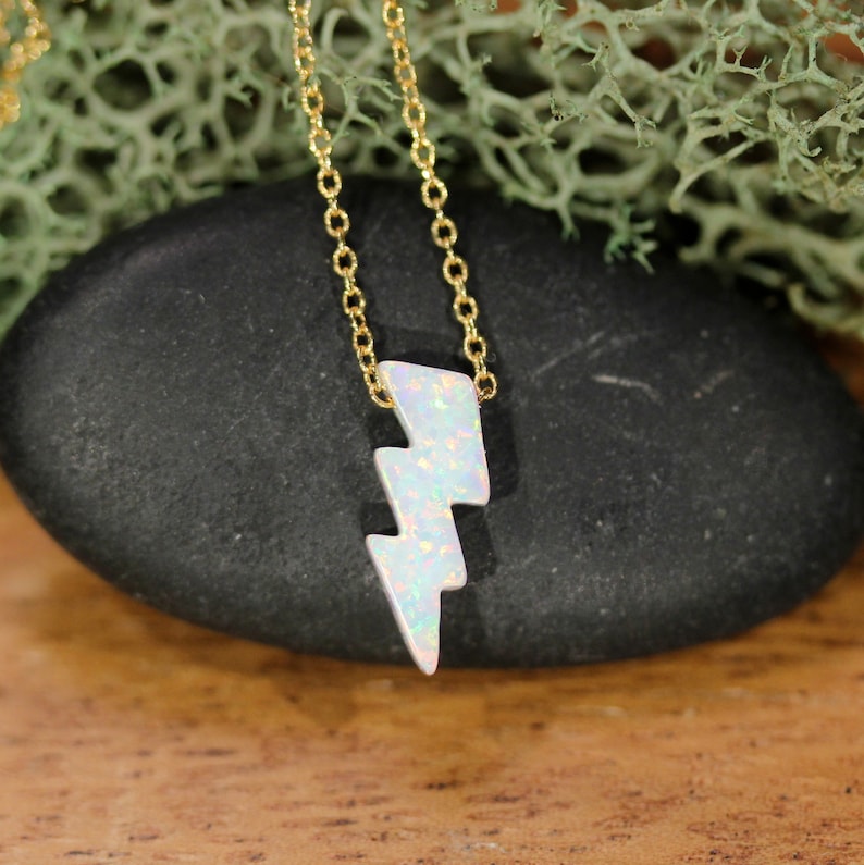 May include: A gold chain necklace with a white opal lightning bolt pendant.