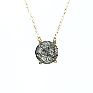 May include: A gold chain necklace with a round, clear quartz pendant with black inclusions. The pendant is set in a gold bezel.