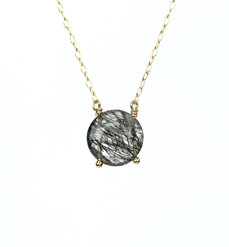 May include: A gold chain necklace with a round, clear quartz pendant with black inclusions. The pendant is set in a gold bezel.