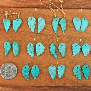 May include: A set of 11 pairs of turquoise leaf earrings with gold hooks. The earrings are arranged in rows on a wooden surface.