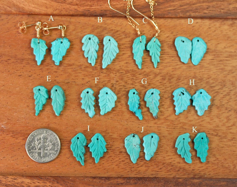 May include: A set of 11 pairs of turquoise leaf earrings with gold hooks. The earrings are arranged in rows on a wooden surface.