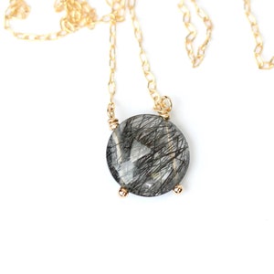 May include: A gold chain necklace with a round, clear quartz pendant with black inclusions. The pendant is set in a gold bezel.