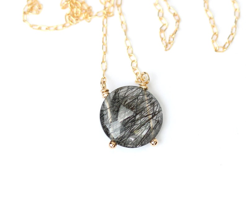 May include: A gold chain necklace with a round, clear quartz pendant with black inclusions. The pendant is set in a gold bezel.
