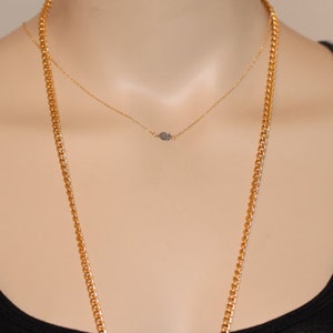 May include: A gold chain necklace with a smaller gold chain necklace layered on top. The smaller chain has a small, sparkly, diamond-shaped pendant.