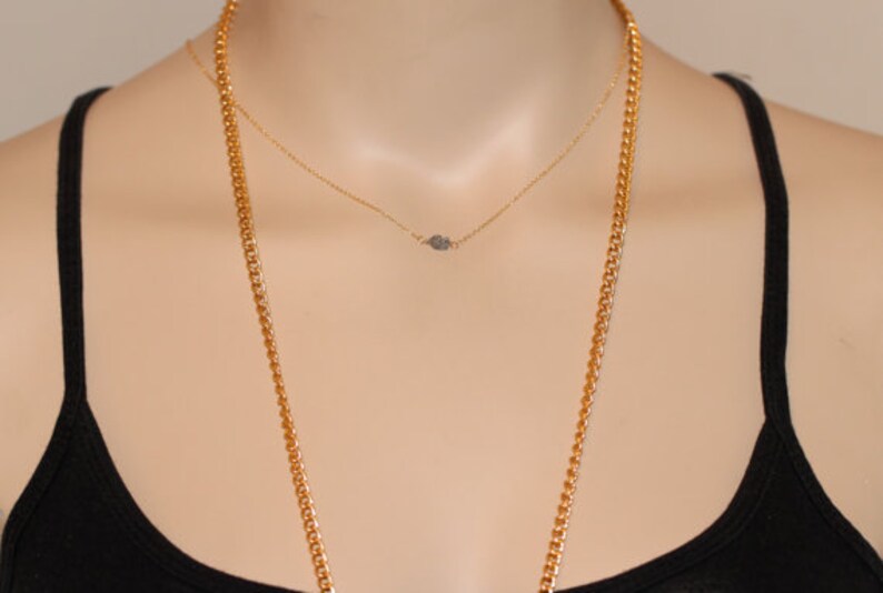 May include: A gold chain necklace with a smaller gold chain necklace layered on top. The smaller chain has a small, sparkly, diamond-shaped pendant.