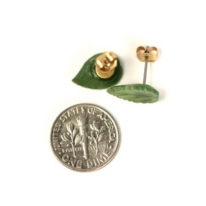May include: A pair of green jade leaf earrings with gold posts. The earrings are about the size of a dime.