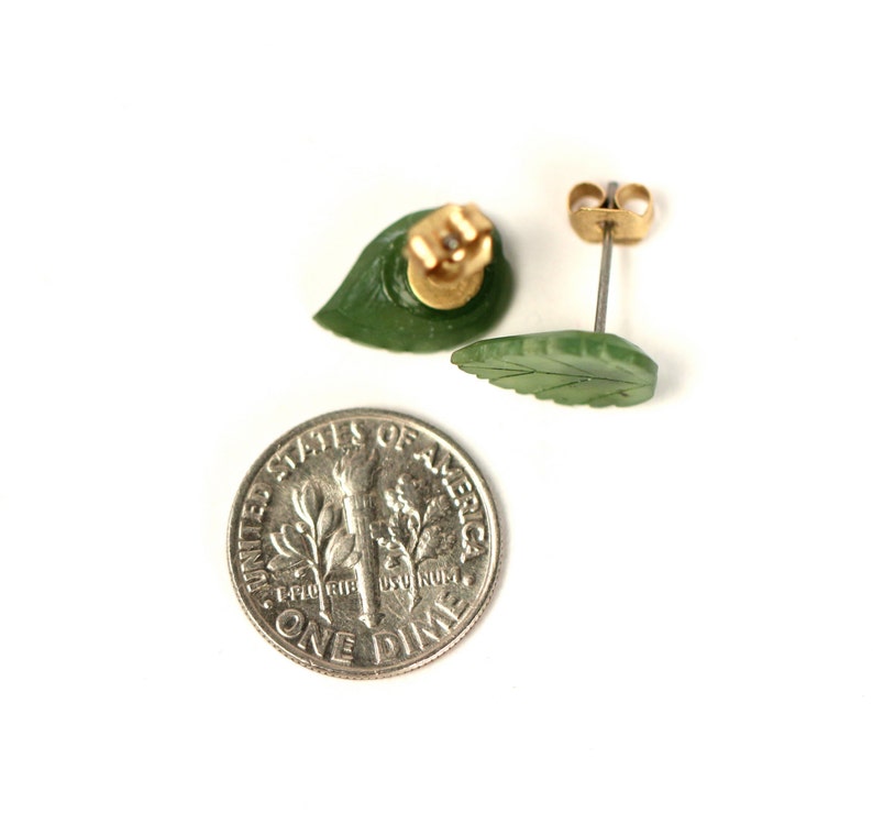 May include: A pair of green jade leaf earrings with gold posts. The earrings are about the size of a dime.