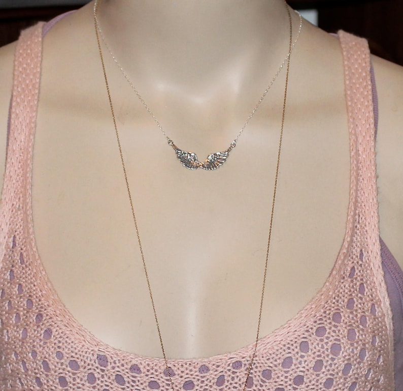 Puede incluir: Un collar de plata con un delicado colgante de ala. El collar est&aacute; superpuesto a una camiseta de tirantes de punto rosa.