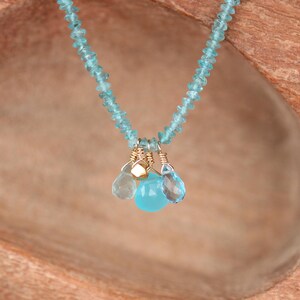 May include: A delicate necklace made with light blue gemstone beads and a pendant featuring three smaller light blue gemstones and a gold accent.