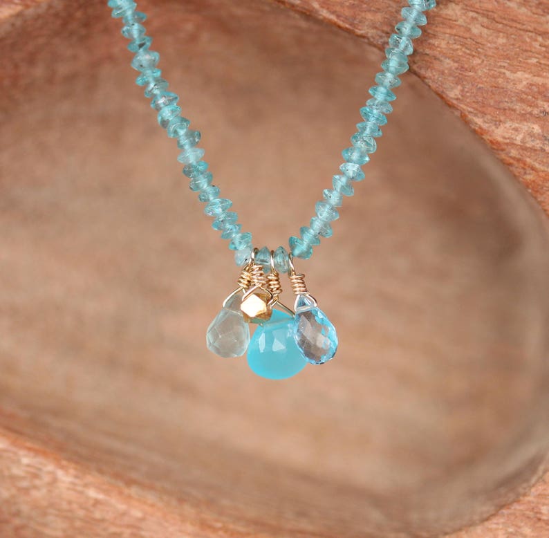 May include: A delicate necklace made with light blue gemstone beads and a pendant featuring three smaller light blue gemstones and a gold accent.