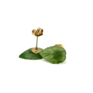 May include: A pair of green jade leaf earrings with gold posts. The leaves are carved with delicate veins and have a natural, organic look.