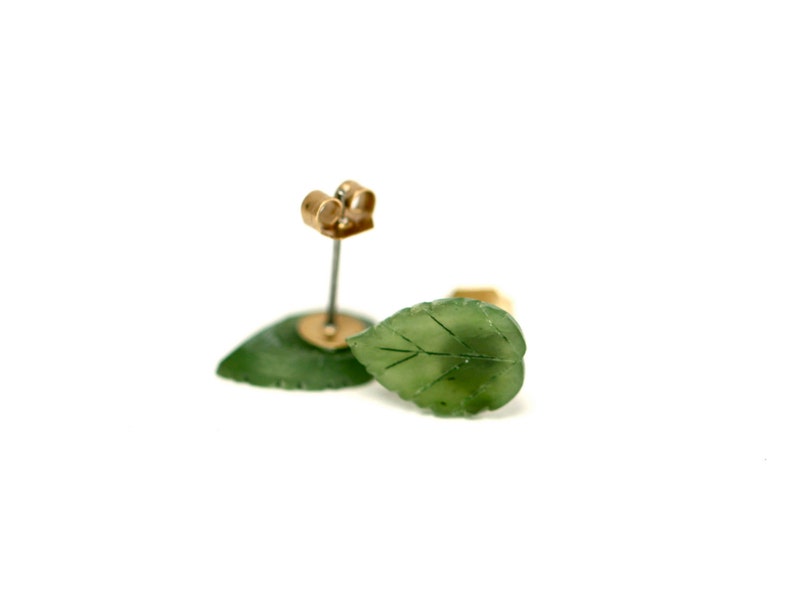 May include: A pair of green jade leaf earrings with gold posts. The leaves are carved with delicate veins and have a natural, organic look.