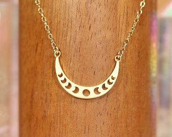 May include: A gold necklace with a crescent moon pendant featuring a cutout design of the moon phases.